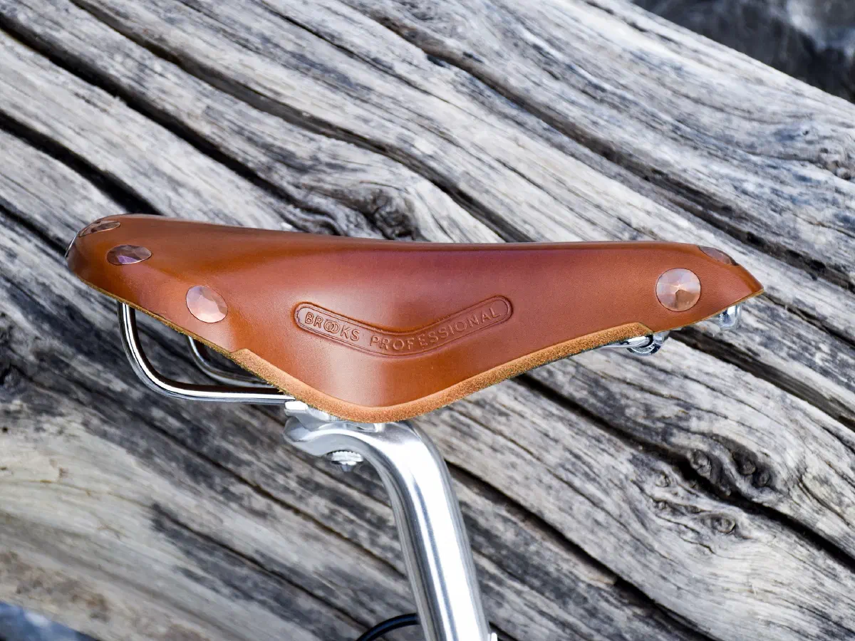 Gros plan sur une selle de vélo en cuir fauve, posée au-dessus de planches de bois patinées.